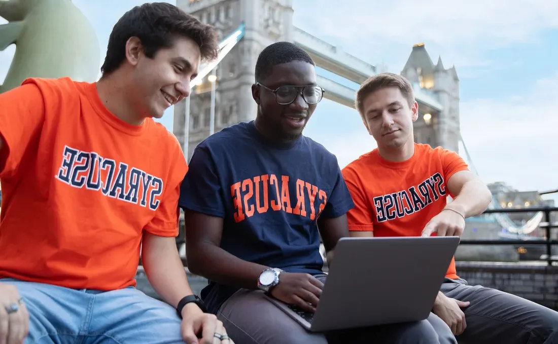 三名身穿雪城大学t恤的学生坐在伦敦桥前.